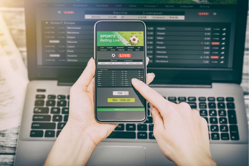 Person betting on sports on smartphone and laptop